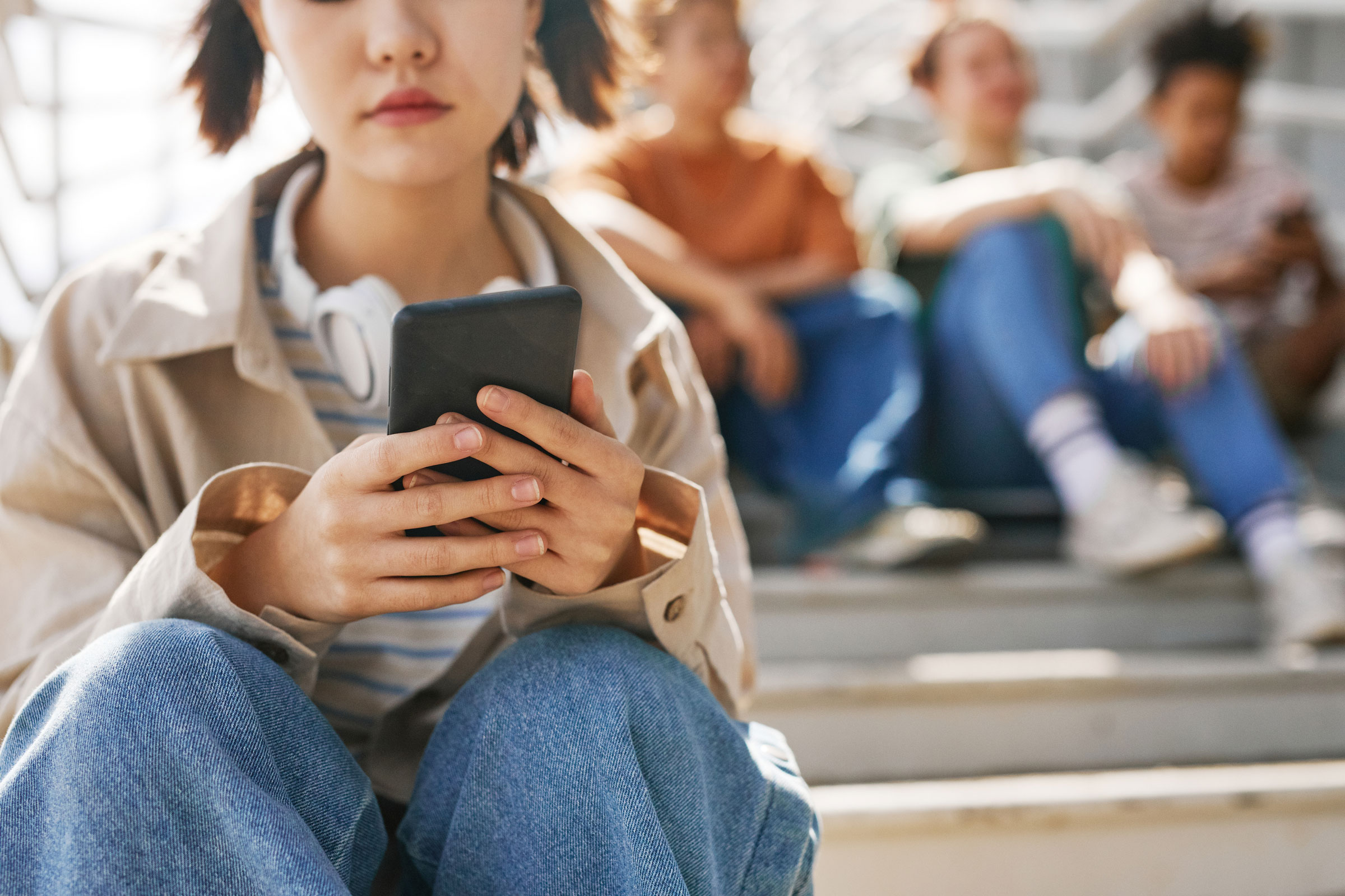 A teenager uses her smartphone with friends sitting in the background.